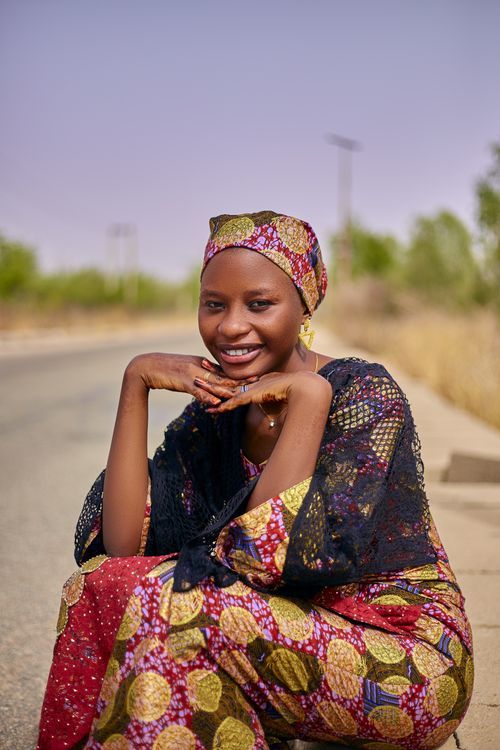 Free A cheerful woman wearing vibrant traditional Nigerian clothing smiles by the roadside. Stock Photo