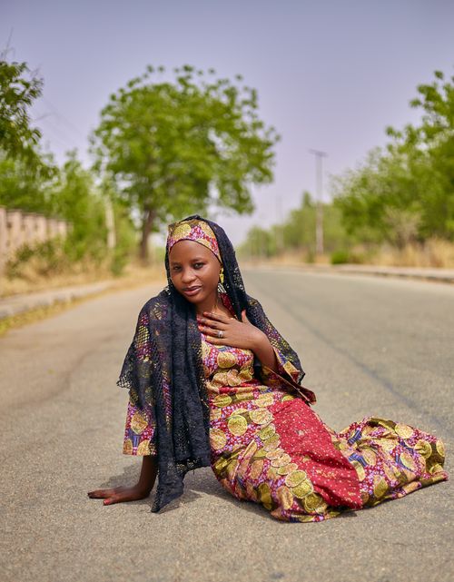 Free Young woman in colorful African attire sitting on a rural road. Stock Photo