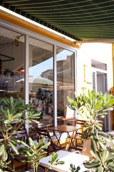 Sunlit café terrace with green awning, chairs, tables, and plants for a cozy outdoor ambiance.