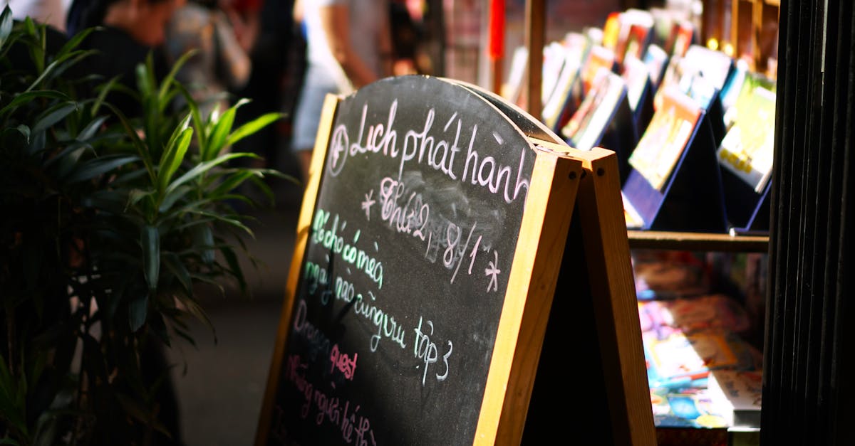 Chalkboard sign at an outdoor market with bustling background and plants.