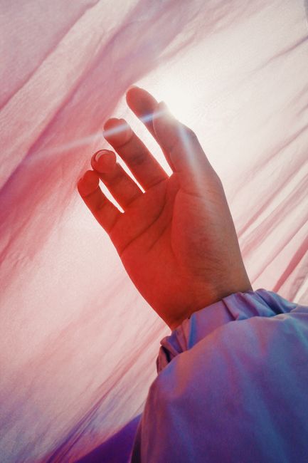An artistic silhouette of a hand under a vibrant cloth with sunlight streaming through creating a dramatic effect.