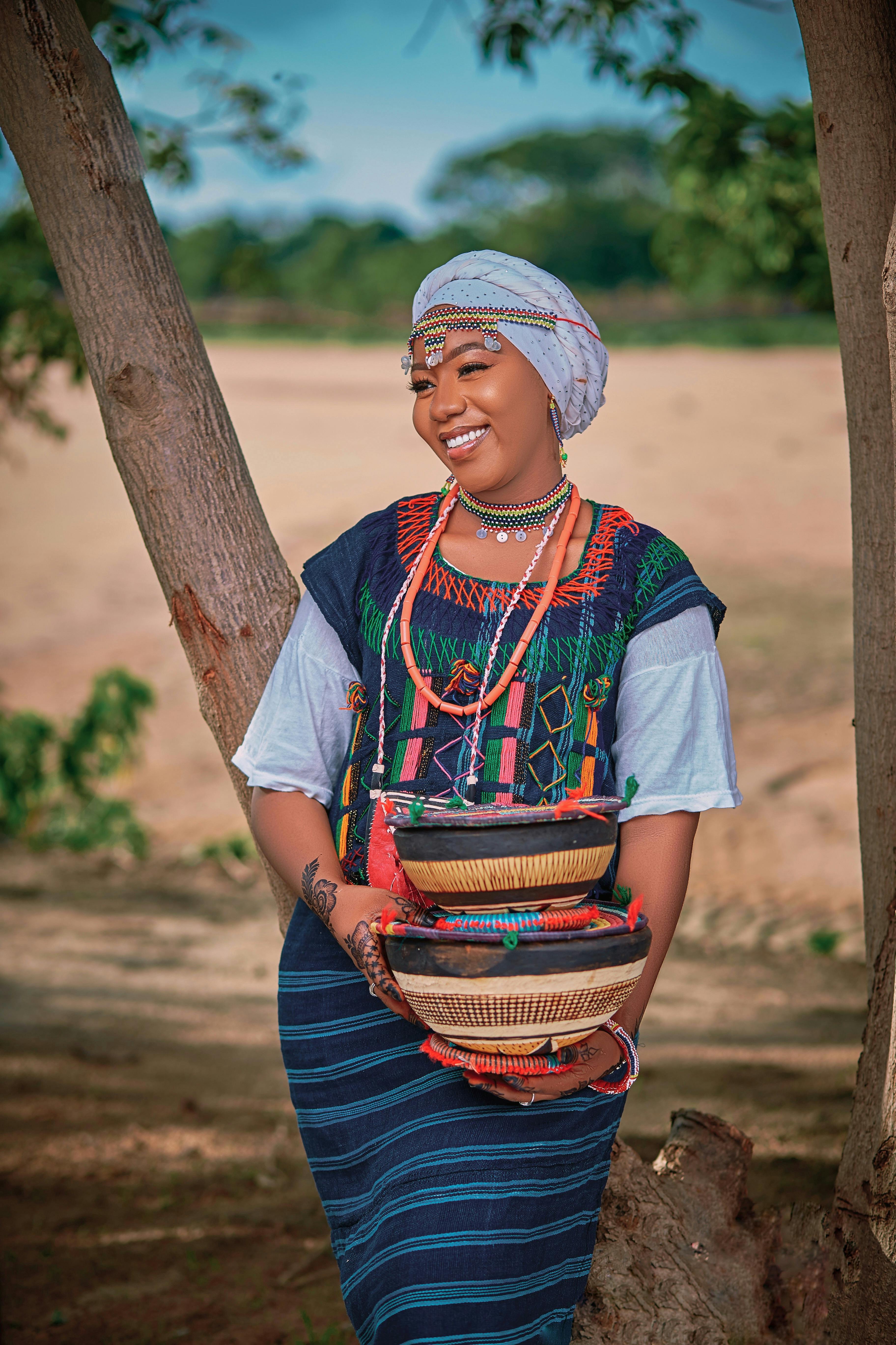 Smiling Nigerian woman in colorful attire holding woven baskets outdoors.