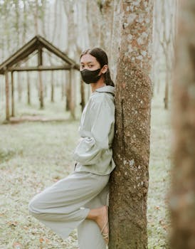 Asian woman wearing a black mask, posing in a serene forest, embodying nature's calm