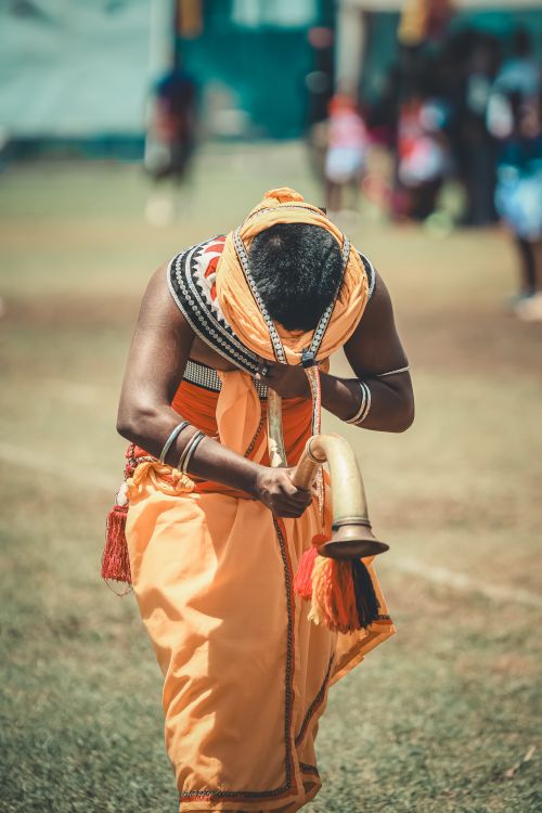 Free A person in traditional attire blowing a horn during a cultural ceremony outdoors. Stock Photo