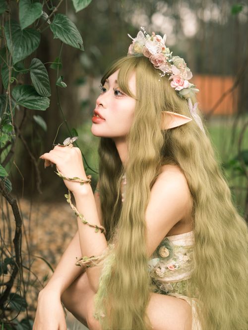 Free Fairy-like woman with flowers in hair posing in a mystical forest setting. Stock Photo