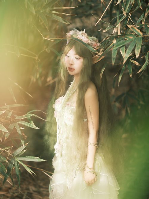 Free A serene portrait of a young woman in a forest, surrounded by greenery, wearing a floral crown. Stock Photo