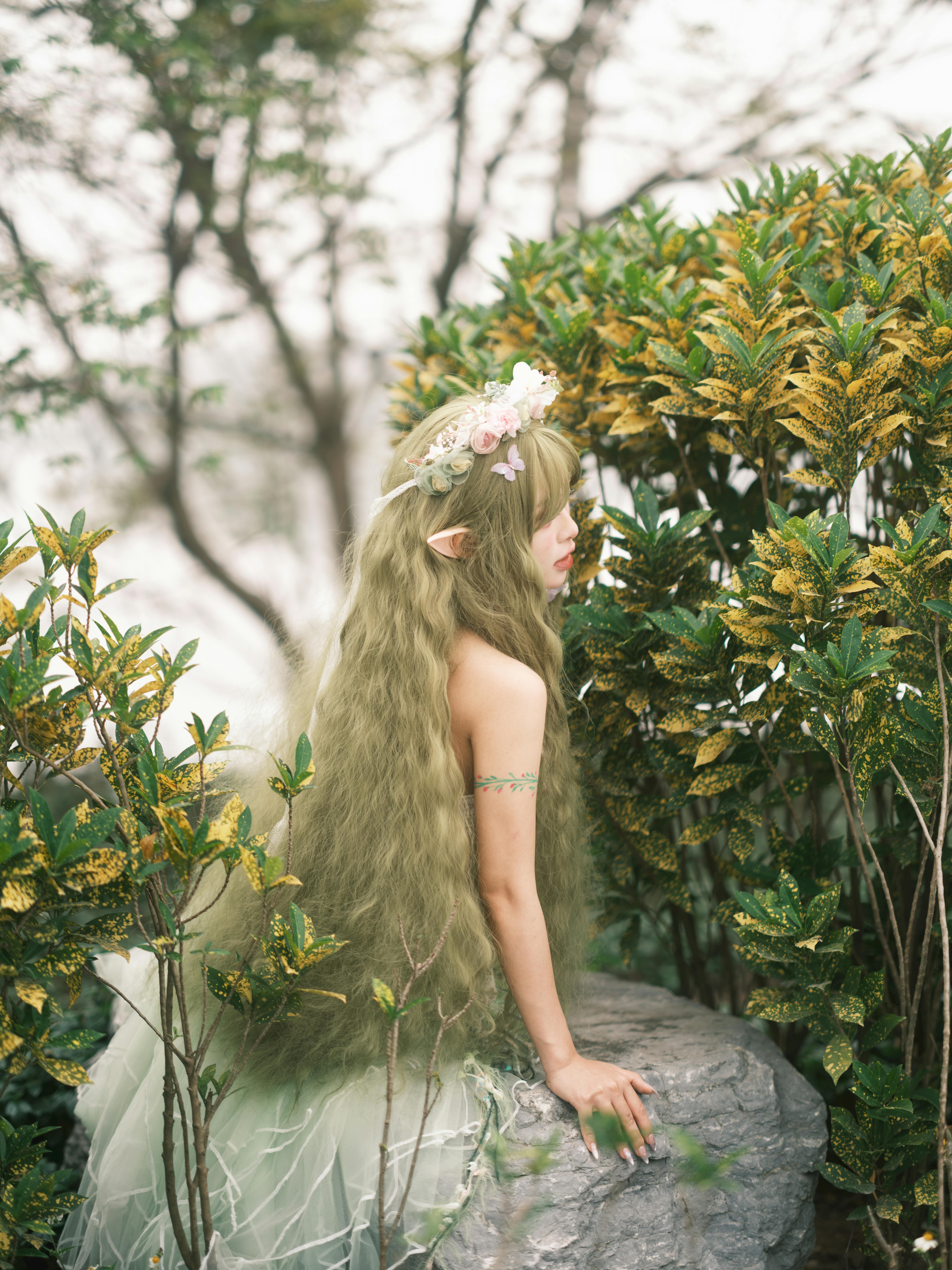 A mystical elf character with a floral crown seated in a vibrant garden.