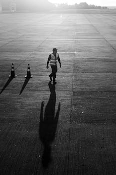 A lone worker walks on an airport tarmac in São Paulo, casting a long shadow.