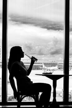 Silhouette of a woman drinking at an airport café with planes in the background.