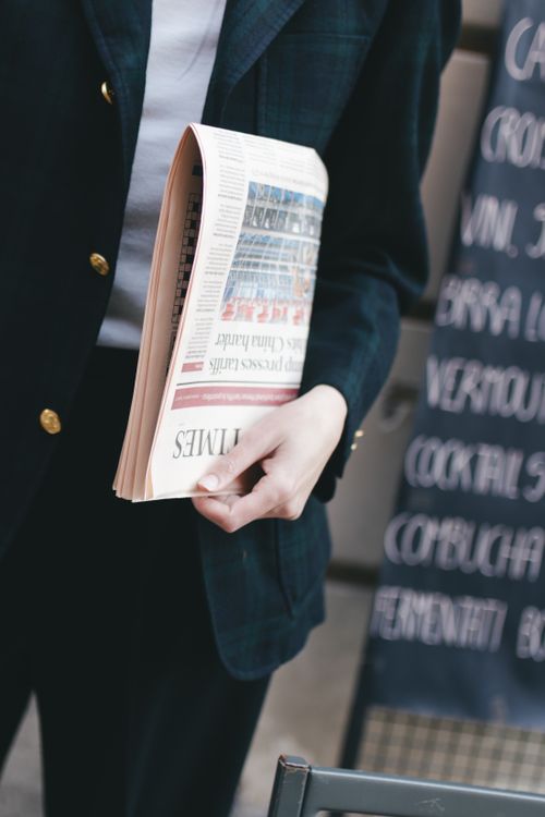 Free A business person in a suit holding a rolled-up newspaper outside a cafe. Stock Photo