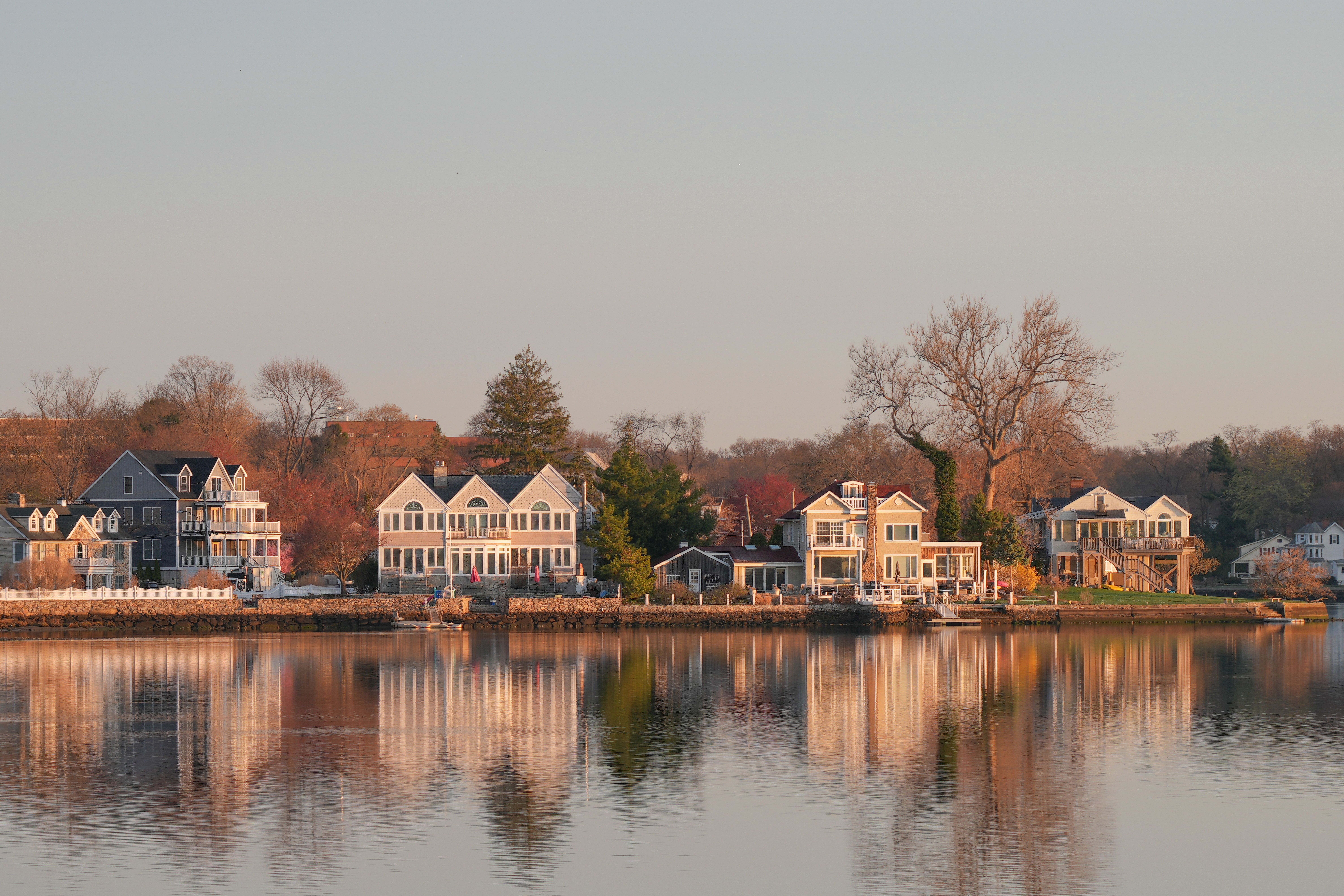 Scenic view of waterfront homes in Stamford, Connecticut at sunrise, with reflections on calm waters.