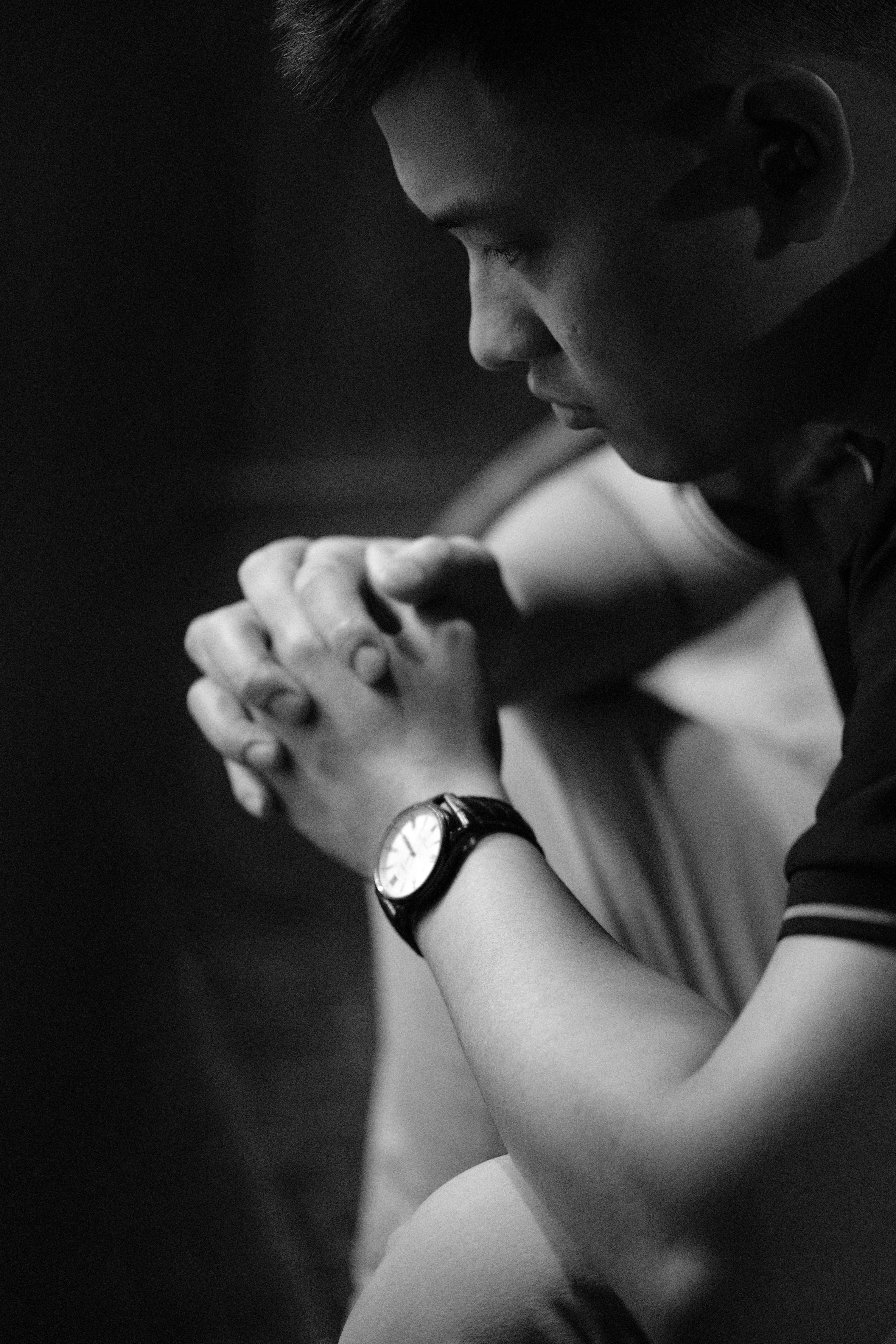 A pensive man sits indoors, focused and deep in thought, in monochrome.