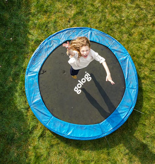 Free A child joyfully jumps on a trampoline in a sunny outdoor garden setting. Stock Photo
