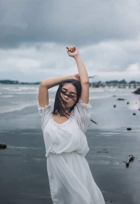 Woman in a white dress posing gracefully on a cloudy beach, capturing the serene coastal atmosphere.