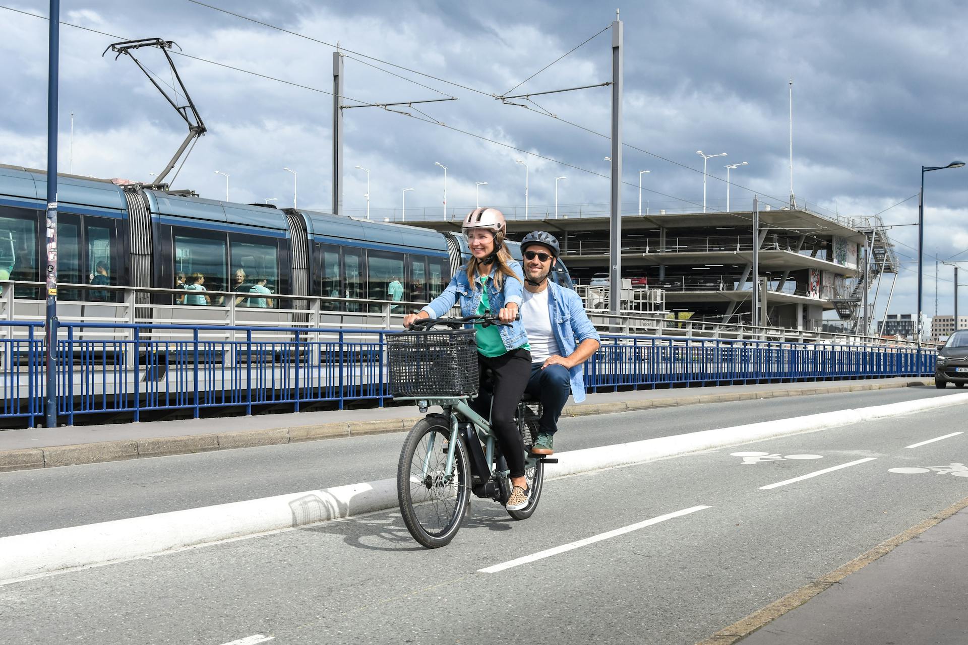 A couple enjoys a sunny ride on a cargo bike in Bordeaux, France, near a tram.