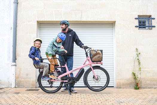 A father and two children wearing helmets ride a pink cargo bike in Paris.