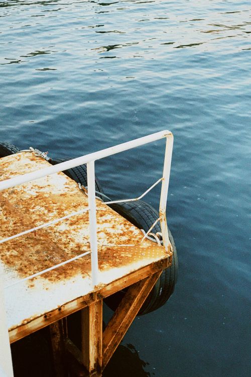 Free A rusty metal dock with a white railing extends over calm blue waters, creating a serene scene. Stock Photo