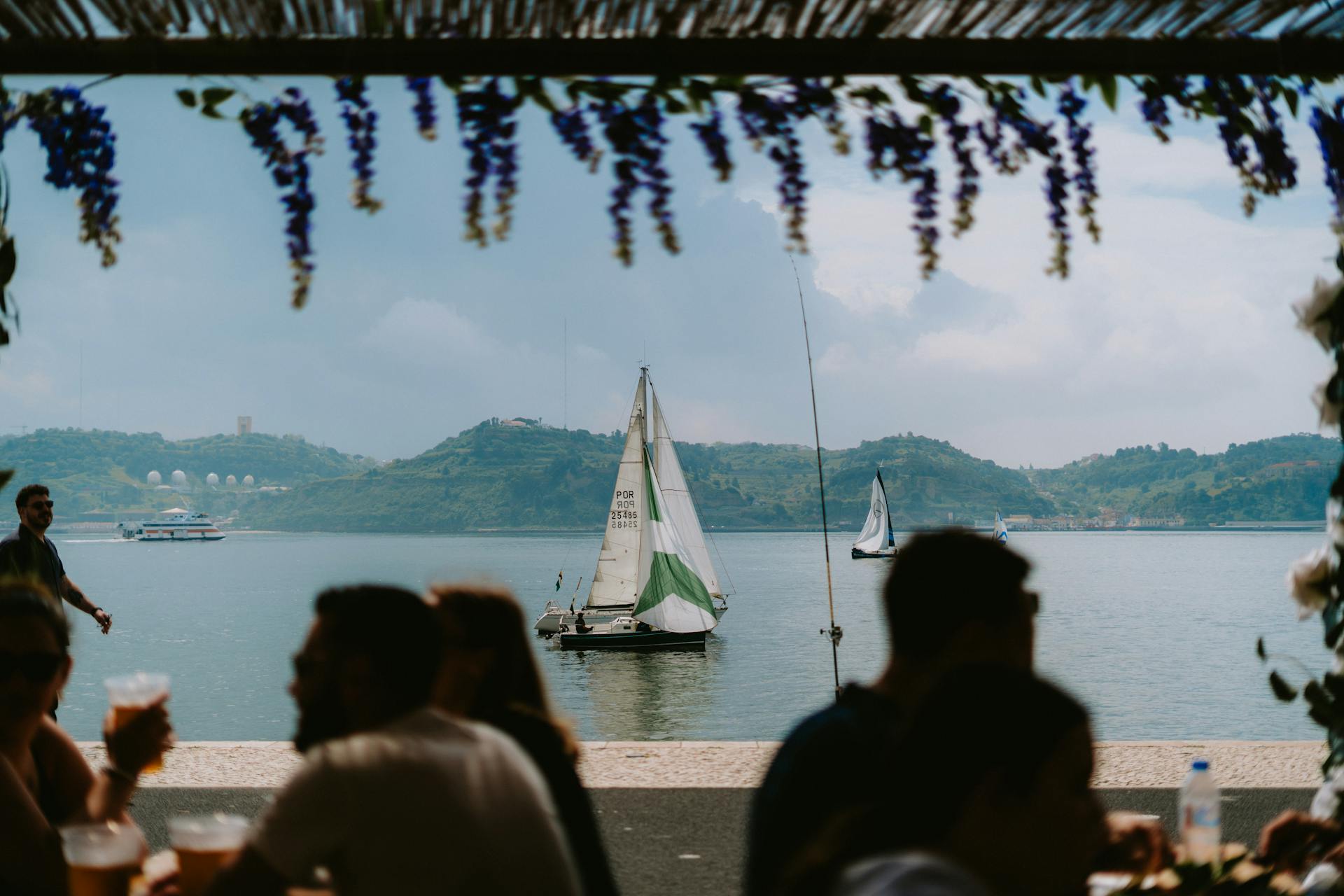 Scenic view of sailboats on the water near Lisbon with people dining in the foreground.