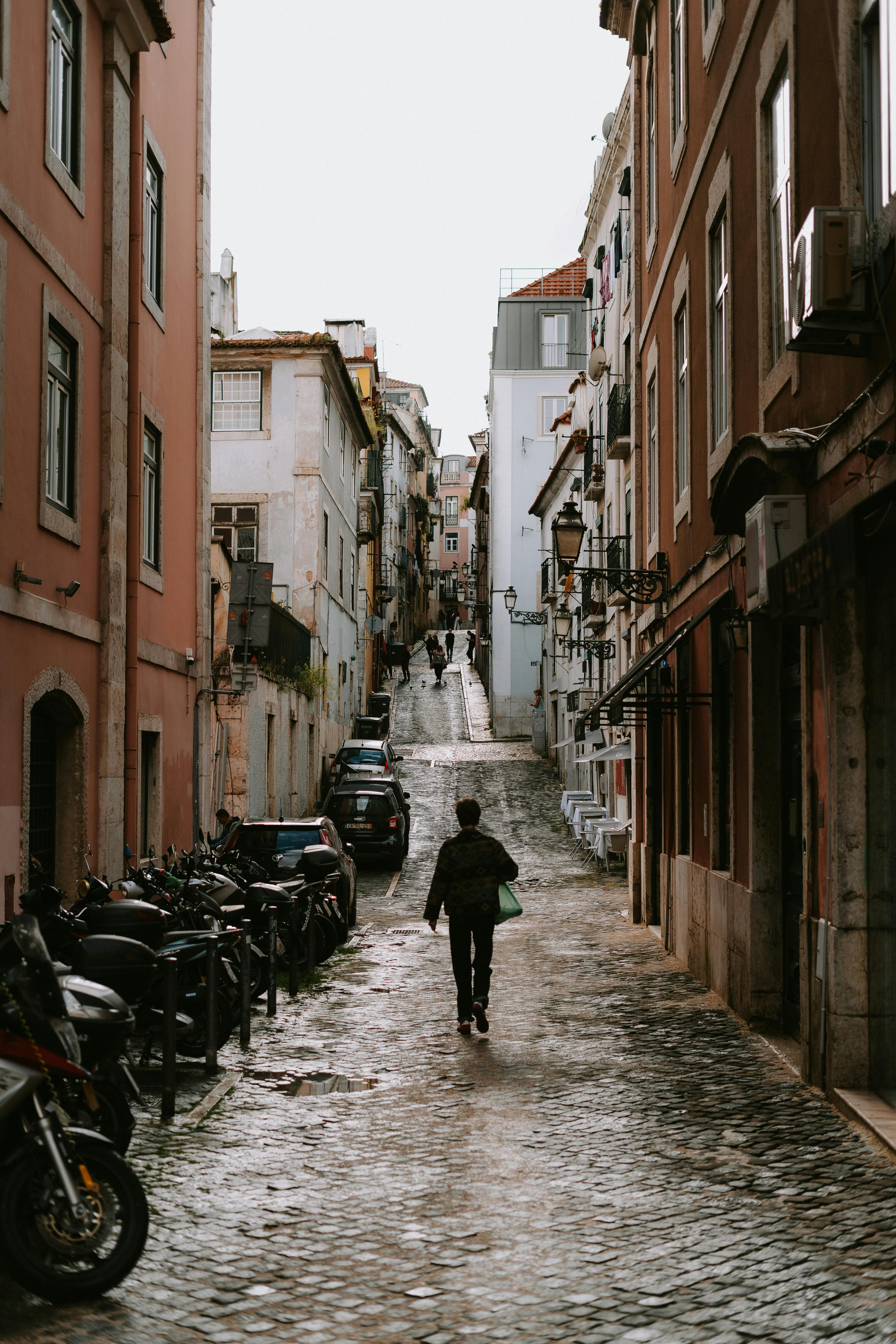 A person walks down a cobblestone street in the historic district of Lisbon, Portugal.
