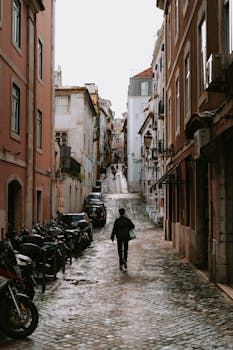 A person walks down a cobblestone street in the historic district of Lisbon, Portugal.