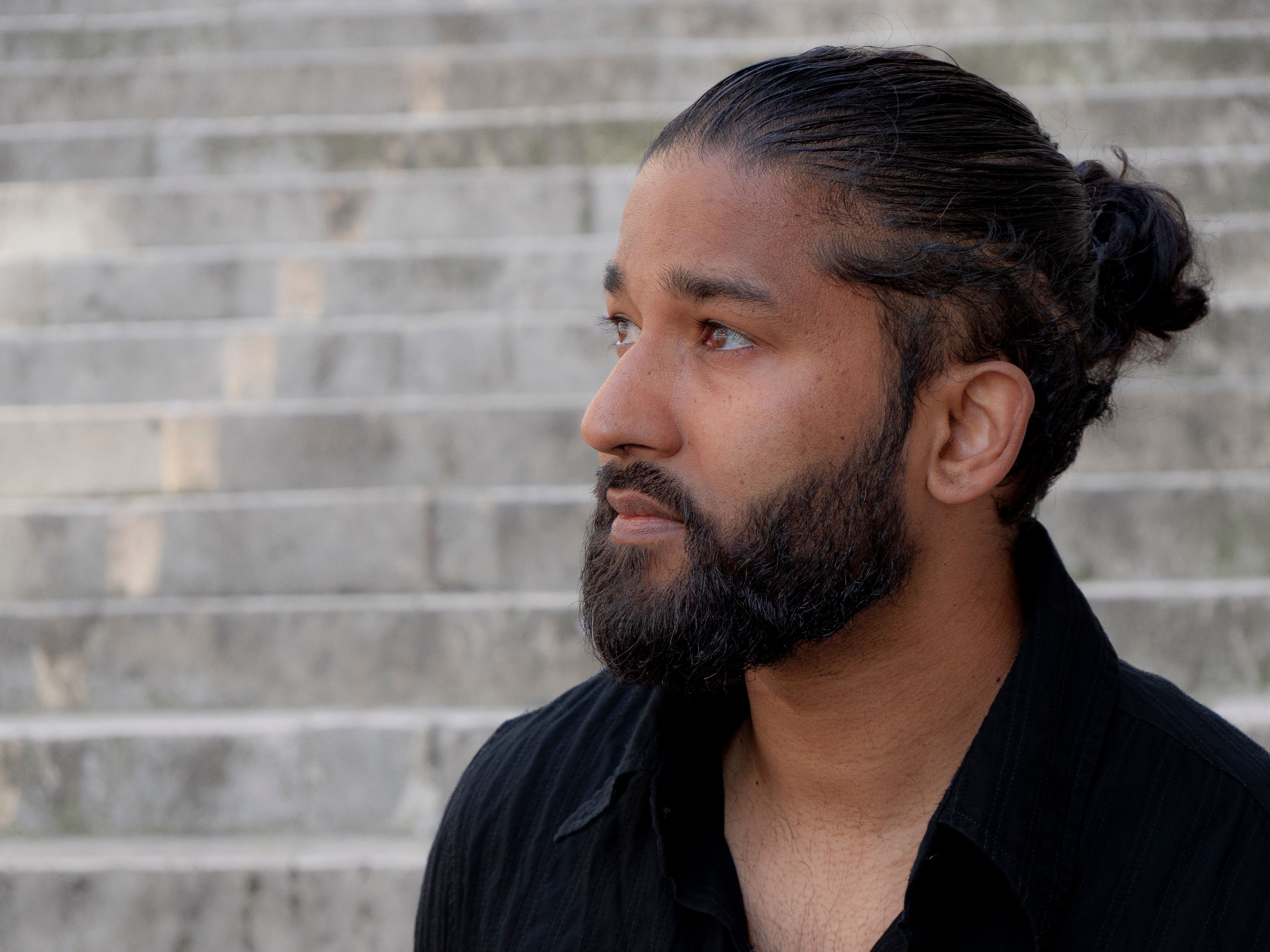 Profile of a bearded man with a bun looking thoughtful on stone steps.