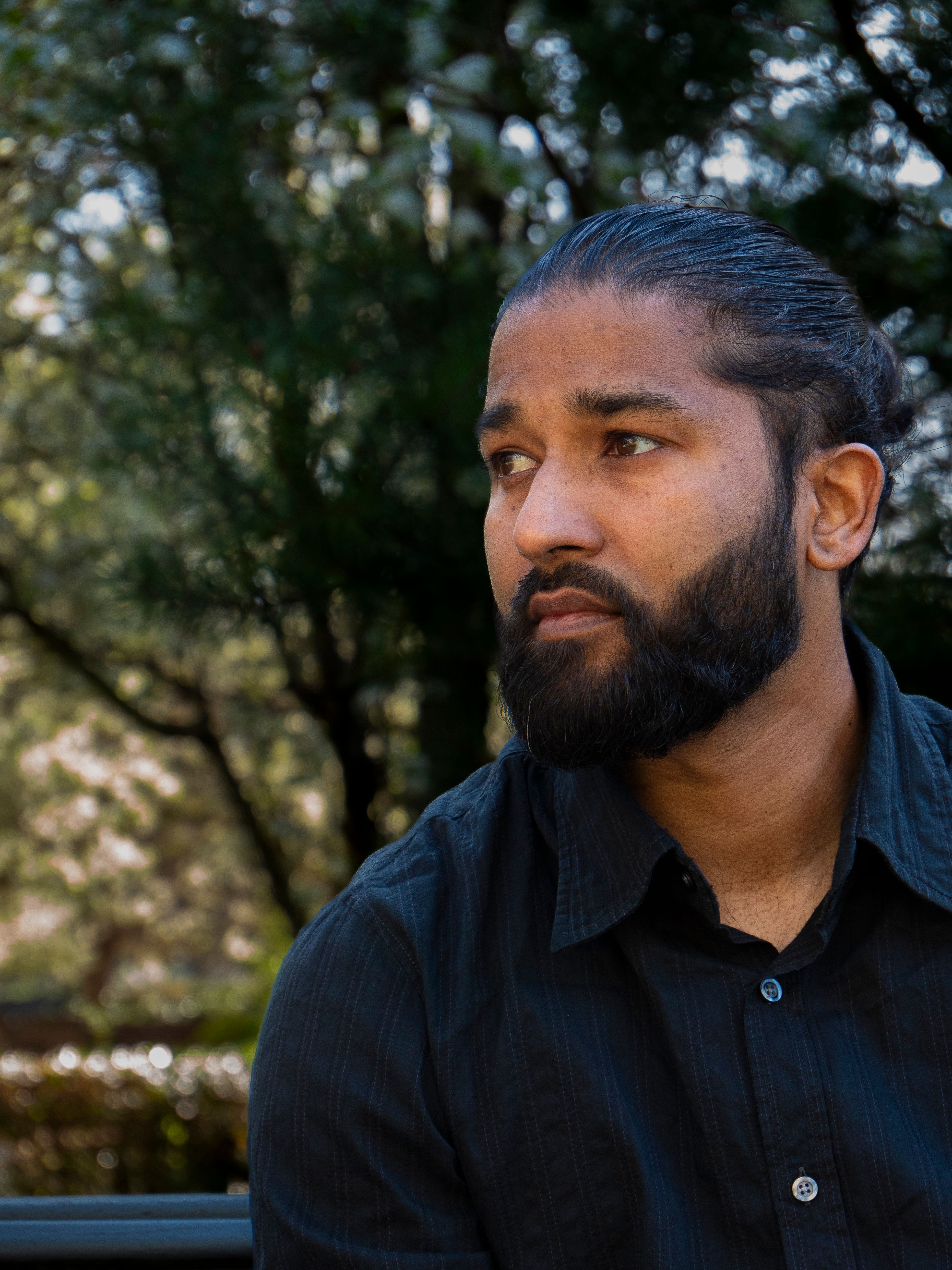 Thoughtful man with beard sitting in sunny park during daytime.