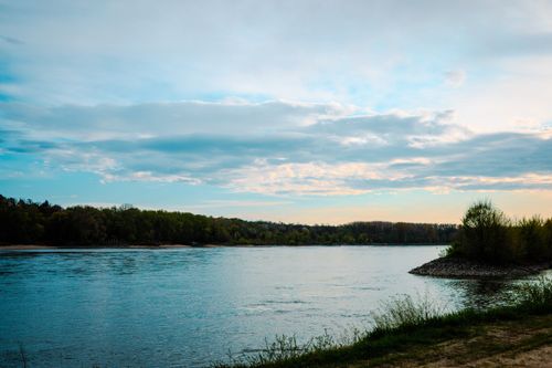 Free A serene landscape of the Danube River in Austria with a lush treeline and vibrant sunset sky. Stock Photo