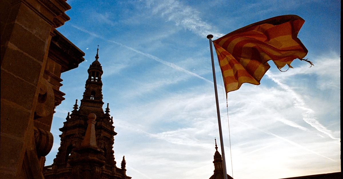 Bandera catalana ondeando con arquitectura histórica contra un cielo vibrante en Barcelona.