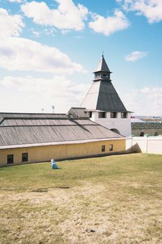 A striking historical tower stands against a bright sky, bordered by a wide green lawn.
