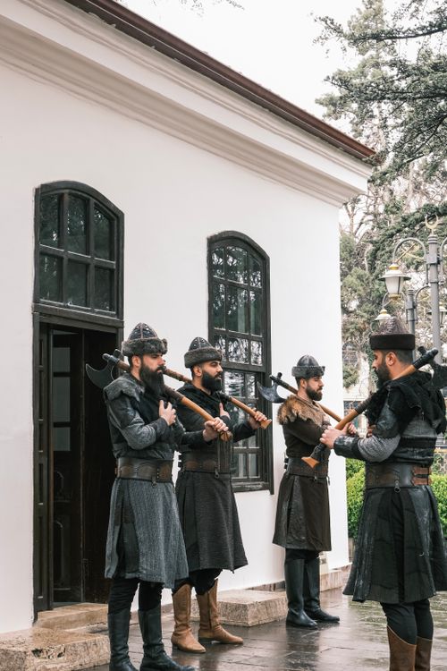 Free Four men in traditional military attire perform outside a historic building. Stock Photo