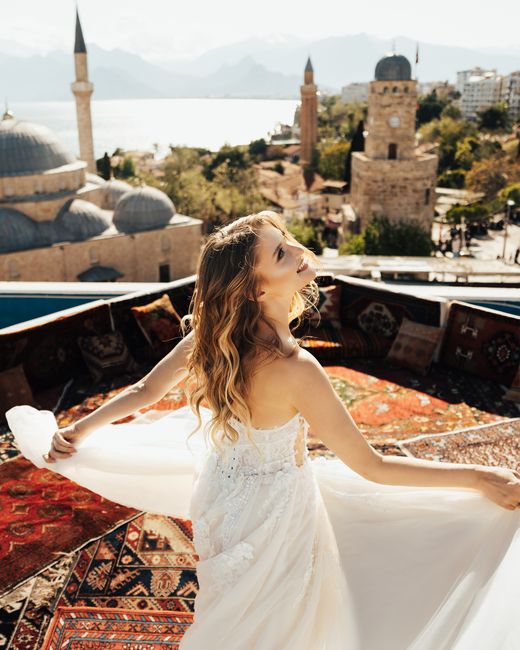 A bride poses on a rooftop with a scenic view of a historic city, domes and towers in the backdrop.
