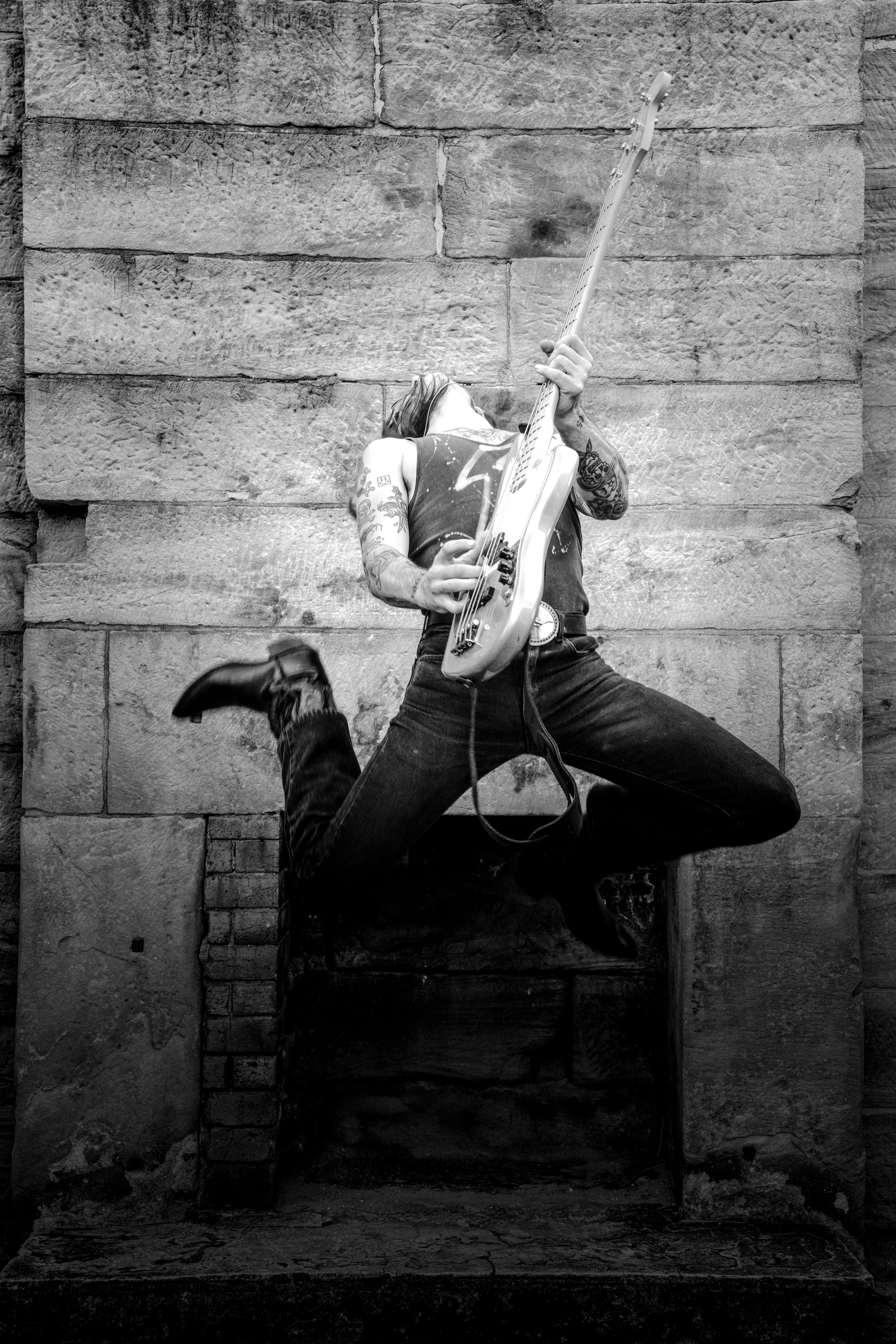 Black and white shot of a guitarist jumping, capturing raw rock energy.