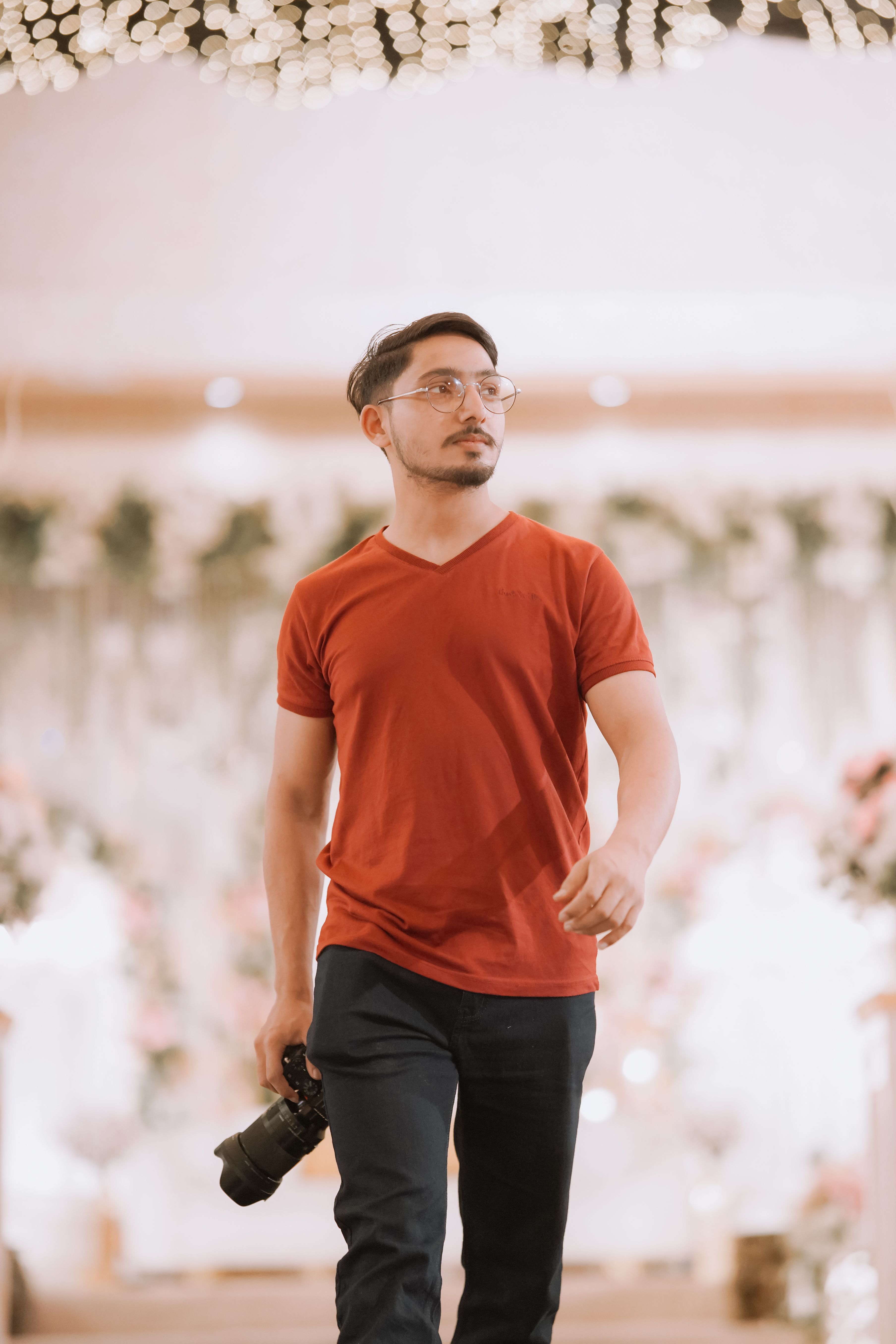 A photographer walks confidently with a camera in a beautifully decorated indoor venue.