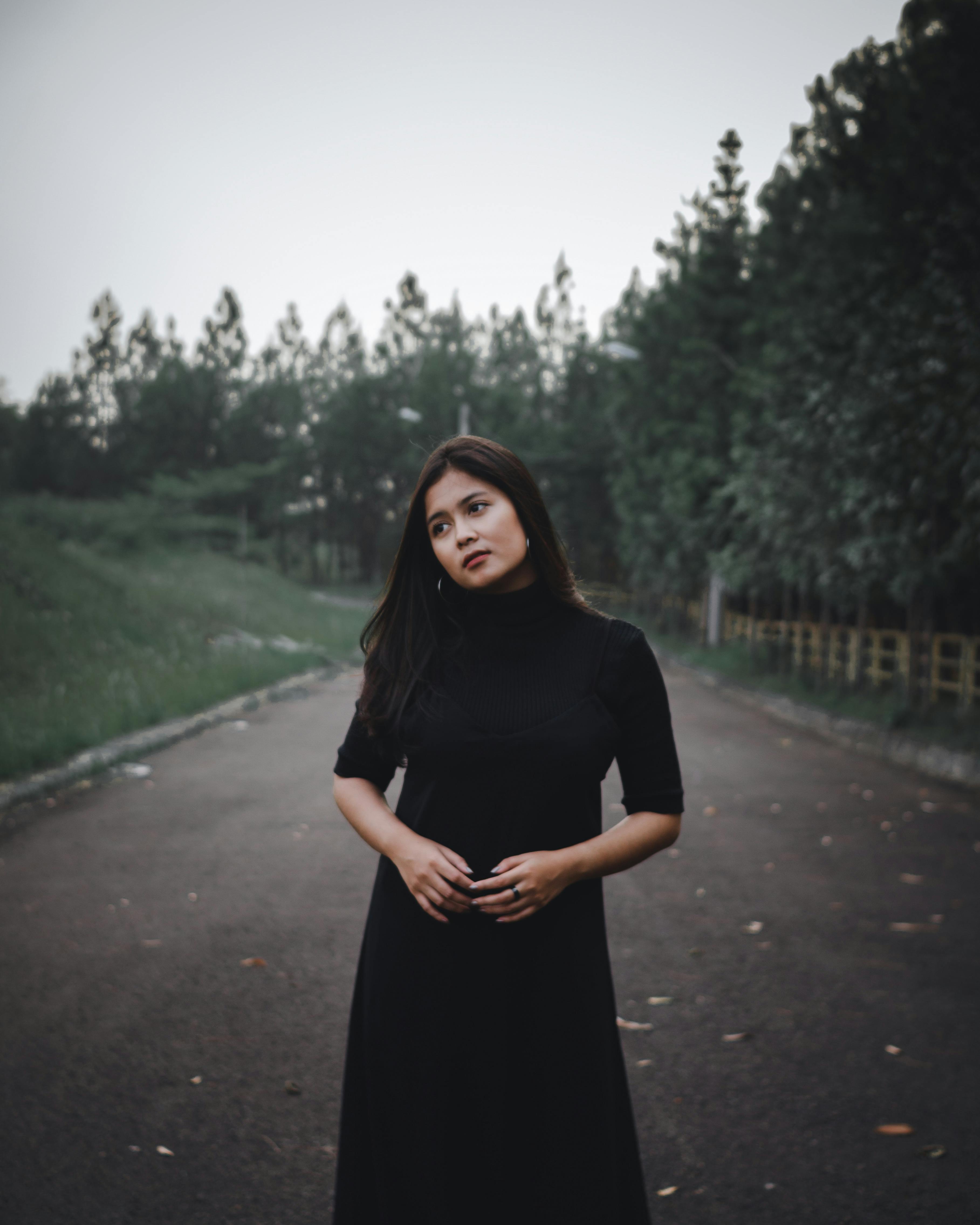 一位体贴的女子身穿黑色连衣裙，站在树木环绕的道路上