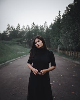 一位体贴的女子身穿黑色连衣裙，站在树木环绕的道路上