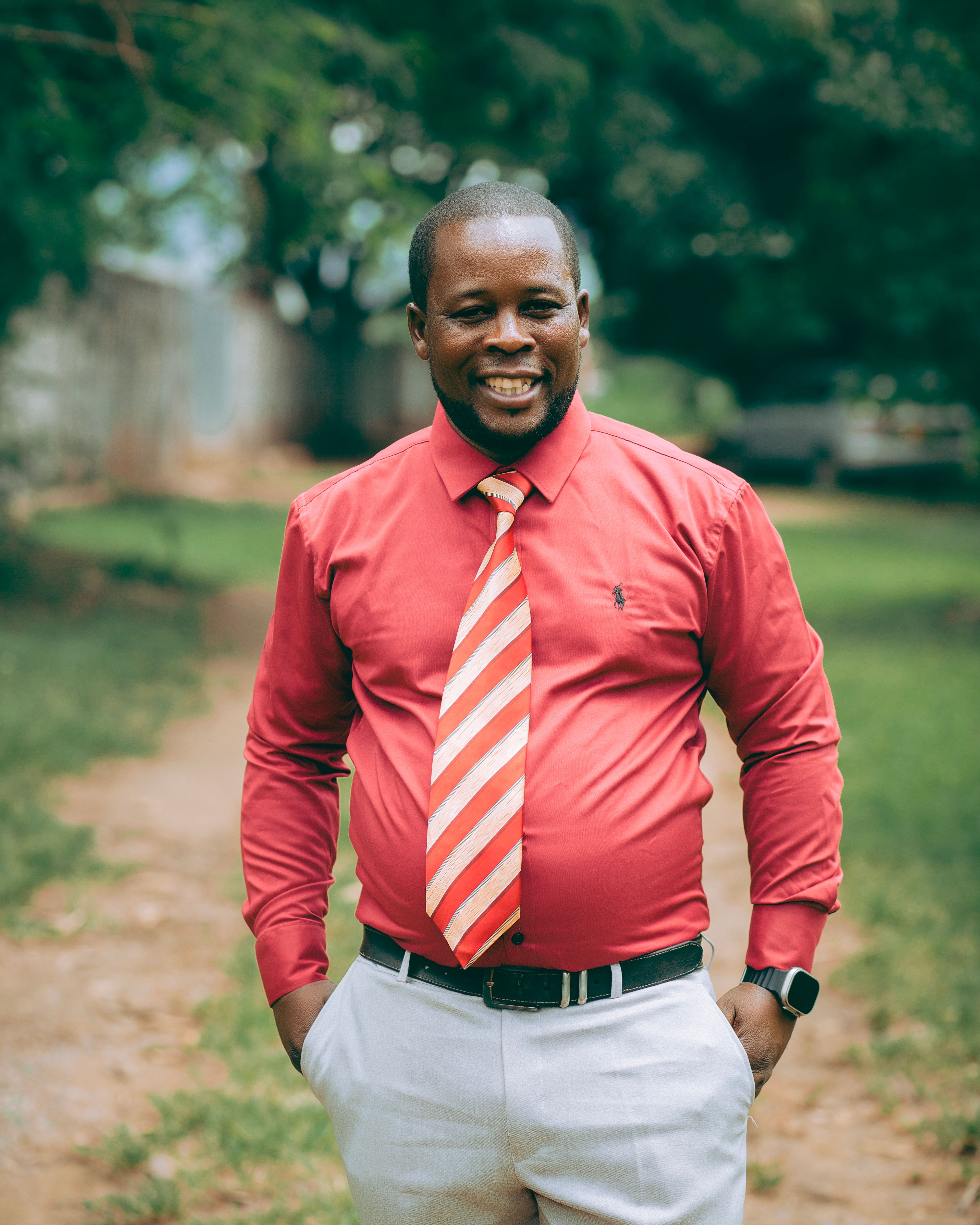 A cheerful man in a red shirt and striped tie smiling outdoors on a sunny day.