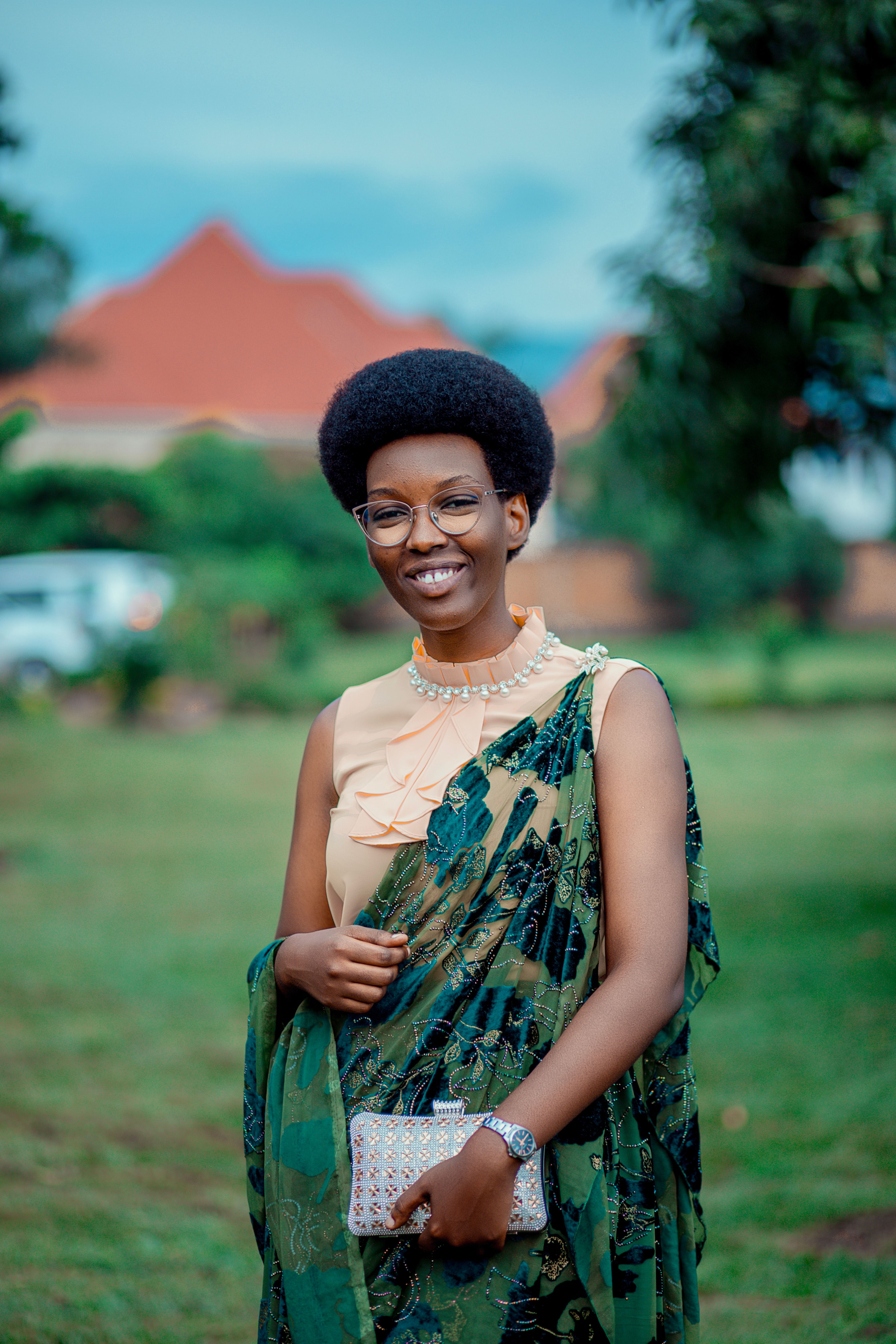 Woman in traditional attire smiling outdoors with a blurred garden background.