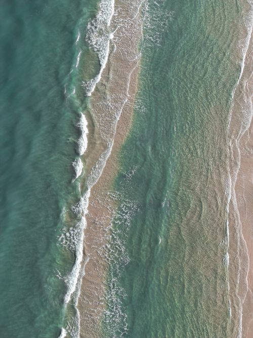 Free Aerial photo capturing the tranquil turquoise waves of a tropical beach, ideal for serene nature visuals. Stock Photo