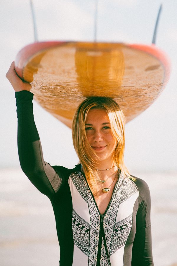 A young female surfer enjoys a sunny day at the beach, holding her surfboard with confidence.