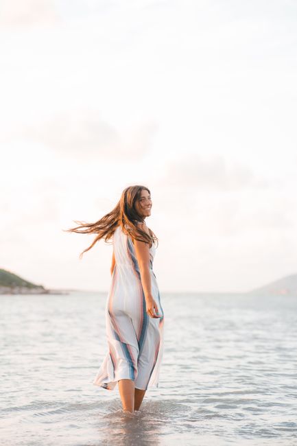 Smiling woman in a dress enjoys a sunny day at the beach, embracing freedom and happiness.