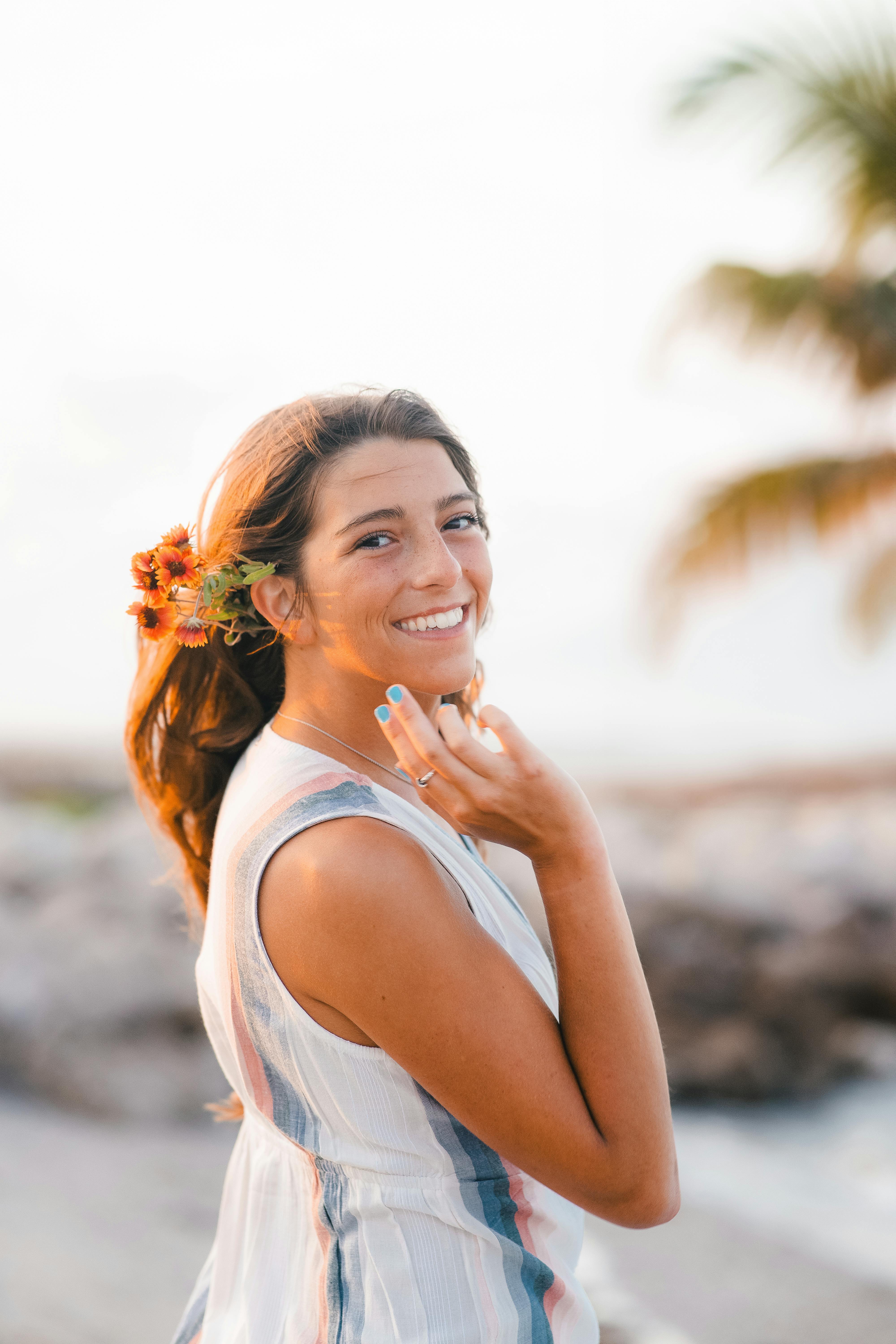 在夏日的黄昏时分，一位头发上插着花的年轻女子在海滩上微笑
