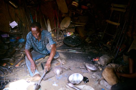 A blacksmith working in a traditional workshop with tools and materials scattered around.