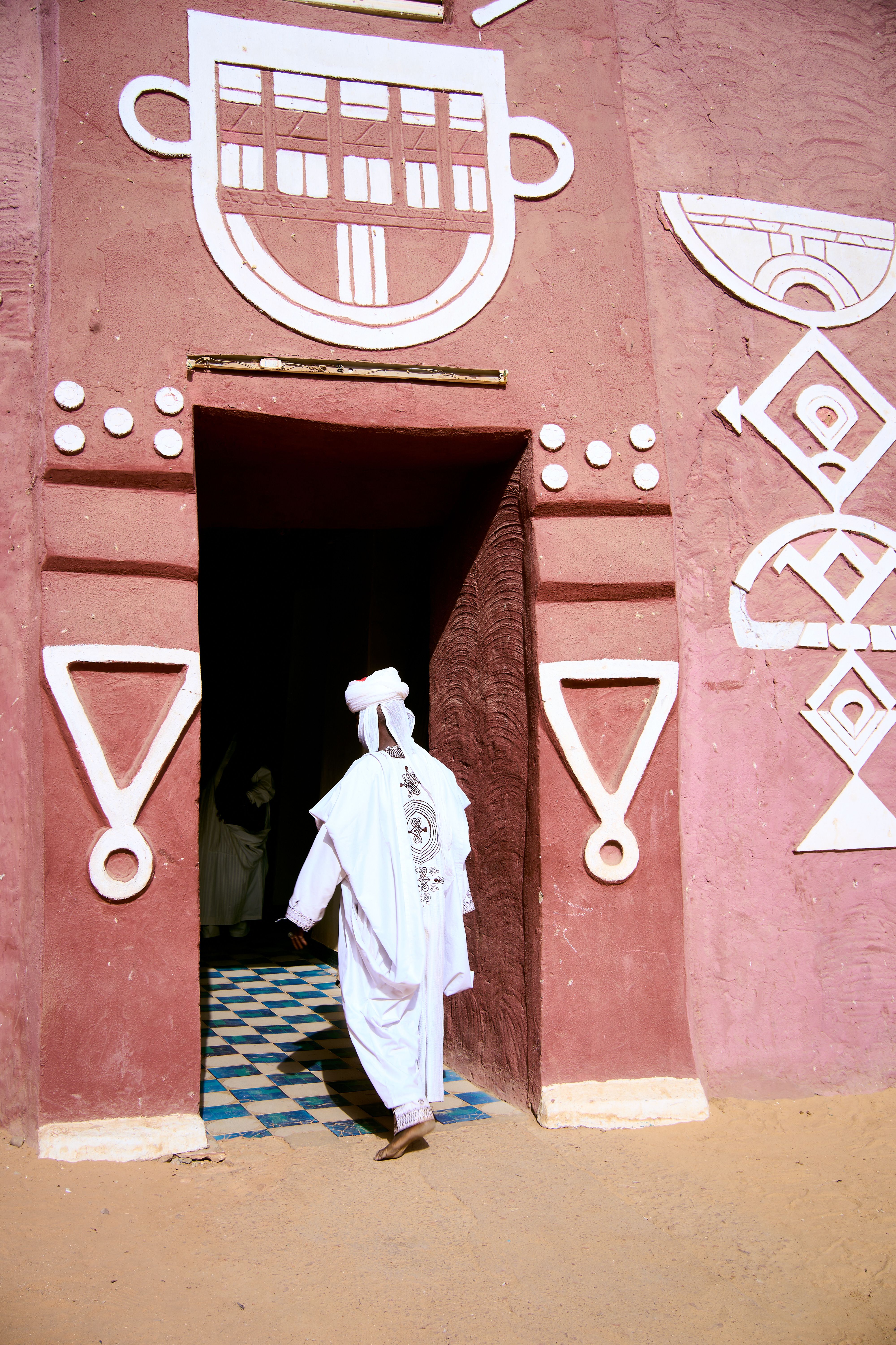 A person enters a decorated African doorway with traditional symbols, wearing a white garment.