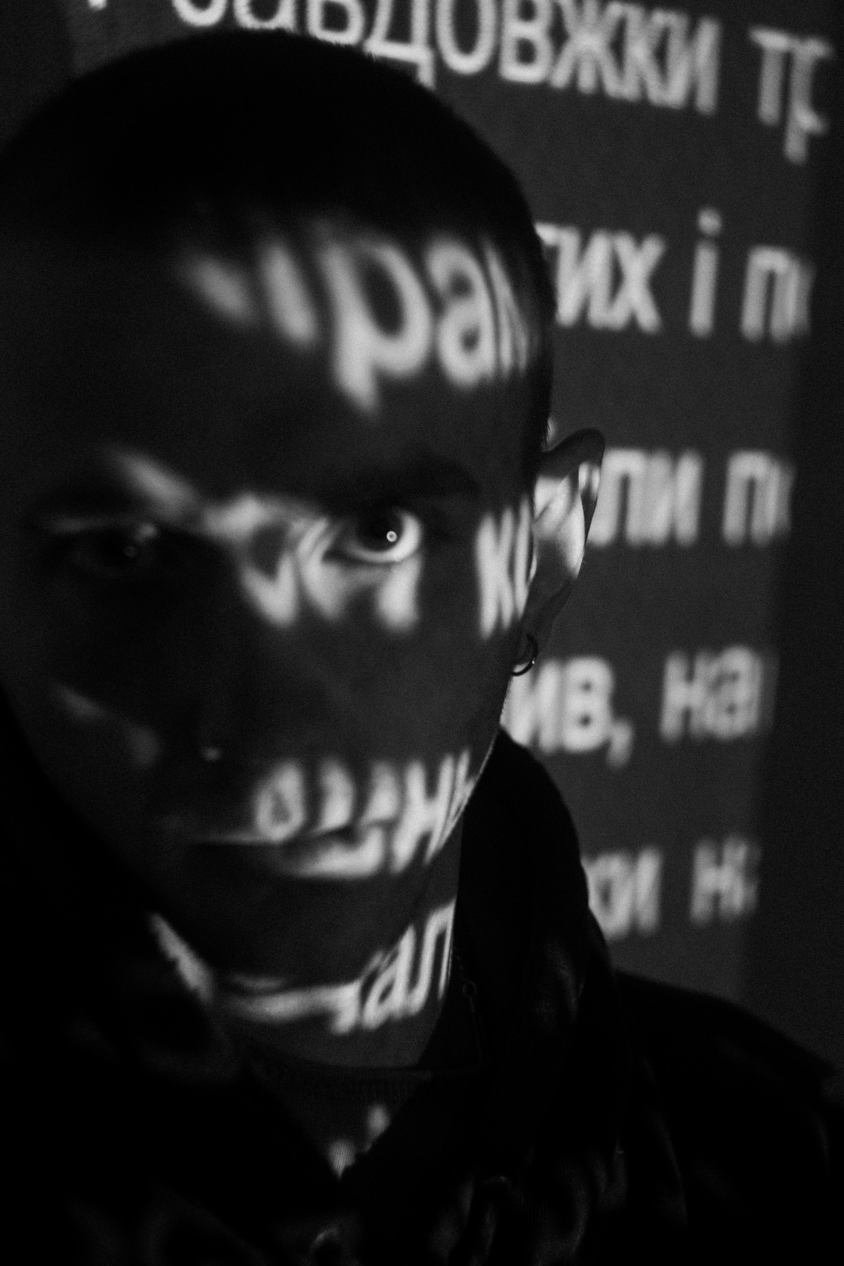 Black and white portrait featuring projected text on a person's face, creating a dramatic shadow effect.