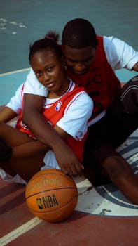 Young couple sitting on a basketball court, embracing and enjoying leisure time.