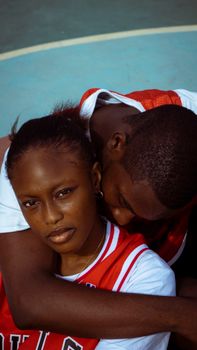 A close-up of a couple in basketball jerseys embracing on an outdoor court.