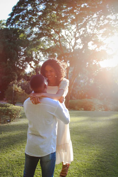 Free A couple shares a romantic embrace in a sunlit garden setting, evoking warmth and love. Stock Photo