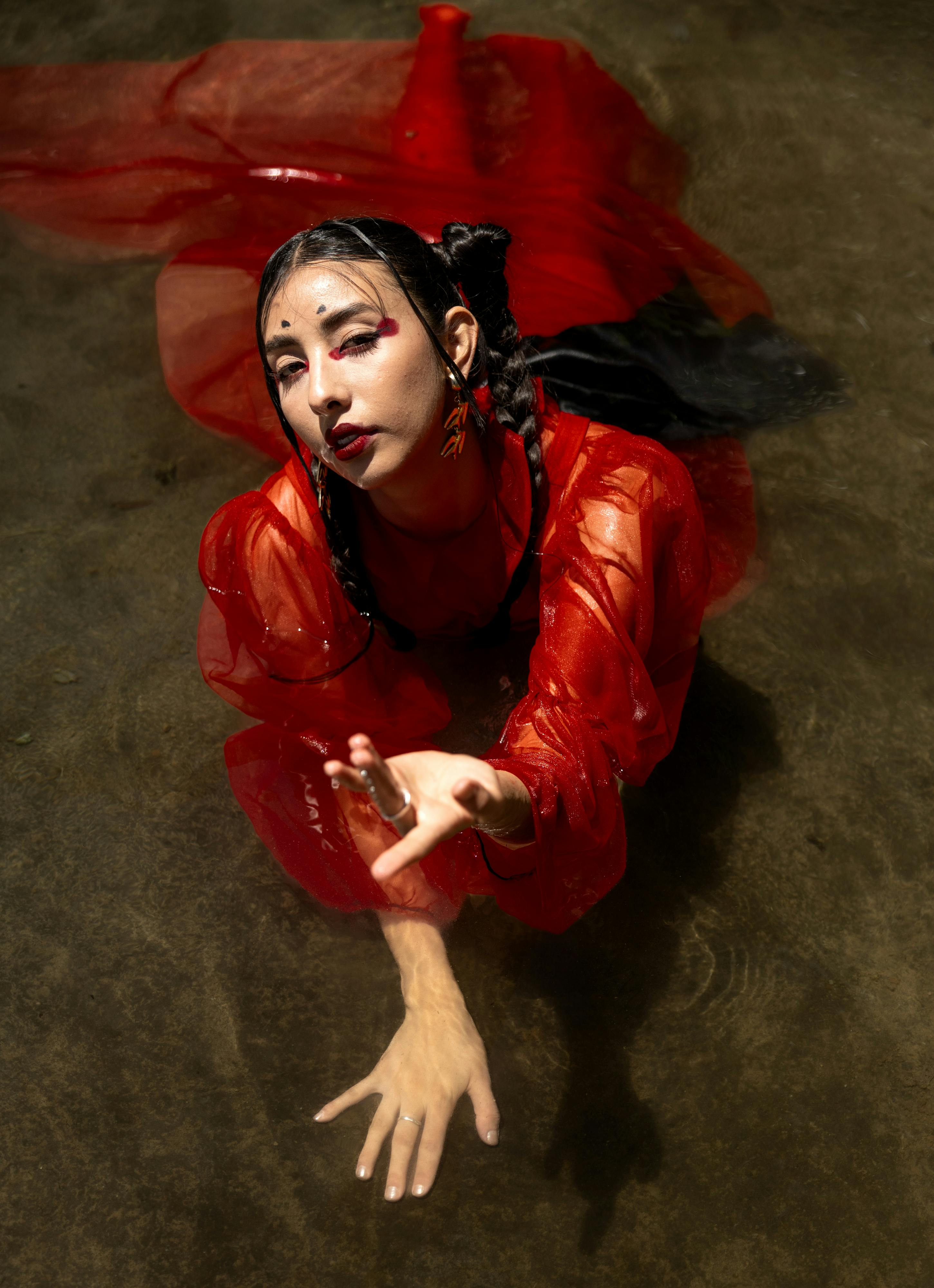 A woman in a red dress poses artistically on a dark floor with dramatic lighting.