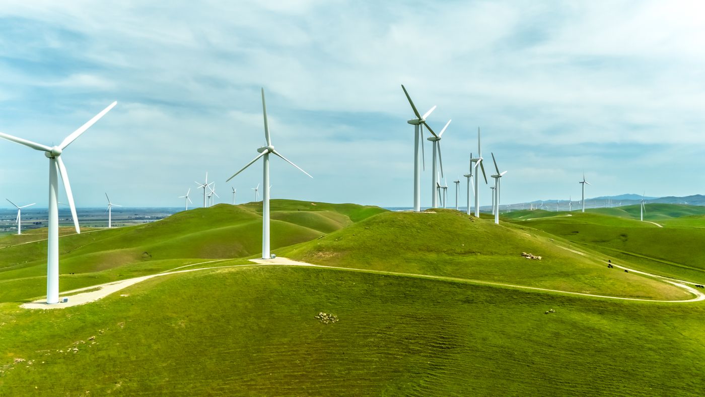 Wind turbines stand tall on lush green hills under a blue sky, generating clean energy in California's landscape.