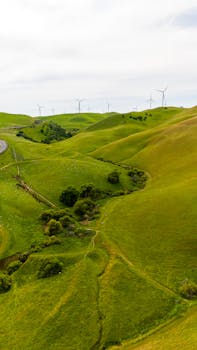 Aerial photograph showcasing wind turbines on lush rolling hills under a cloudy sky, perfect for renewable energy concepts.